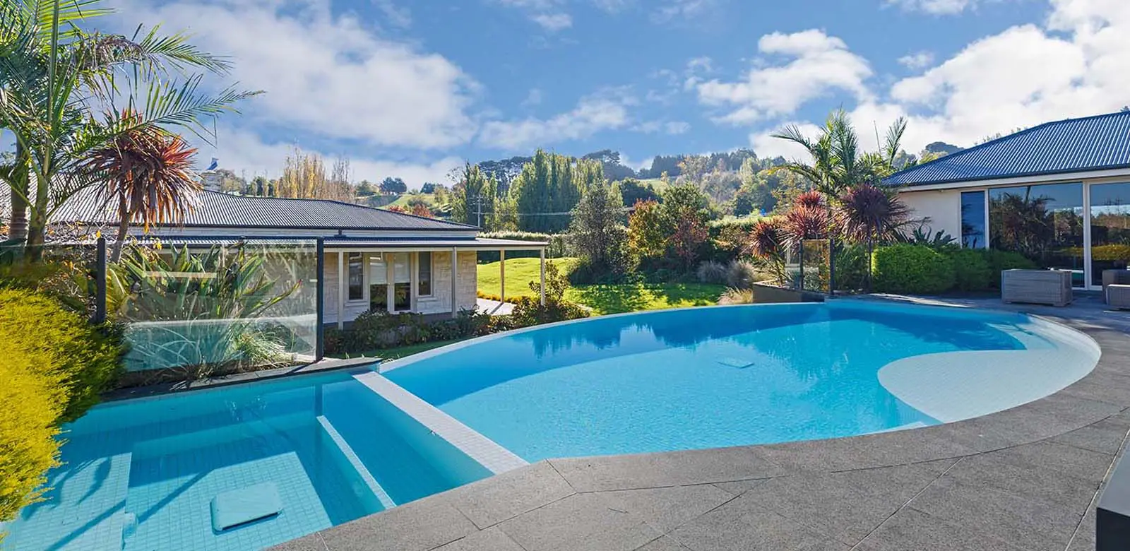 Negative edge pool in backyard with house and trees, creating a serene atmosphere